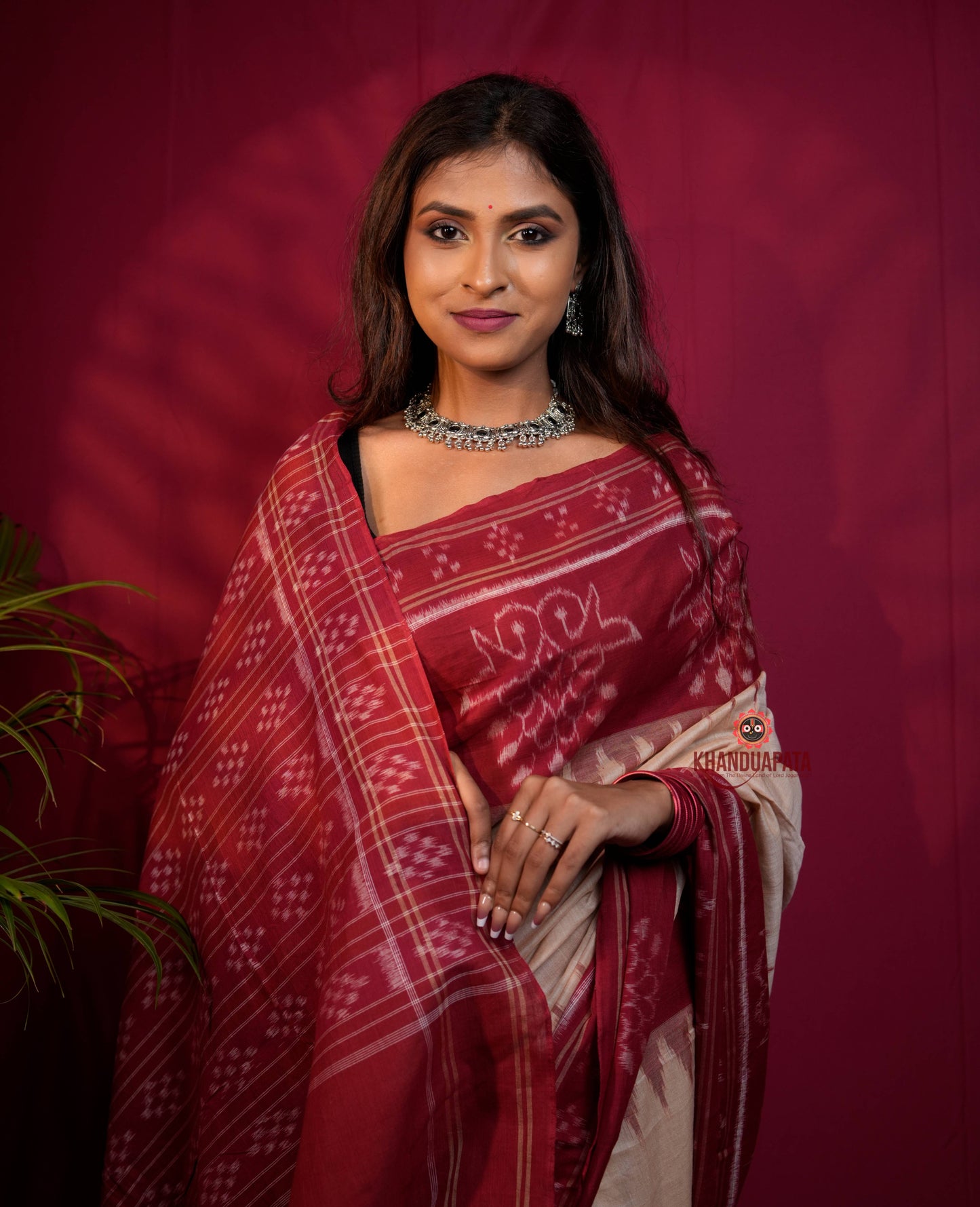 Woman wearing a red and white saree with a maroon background
