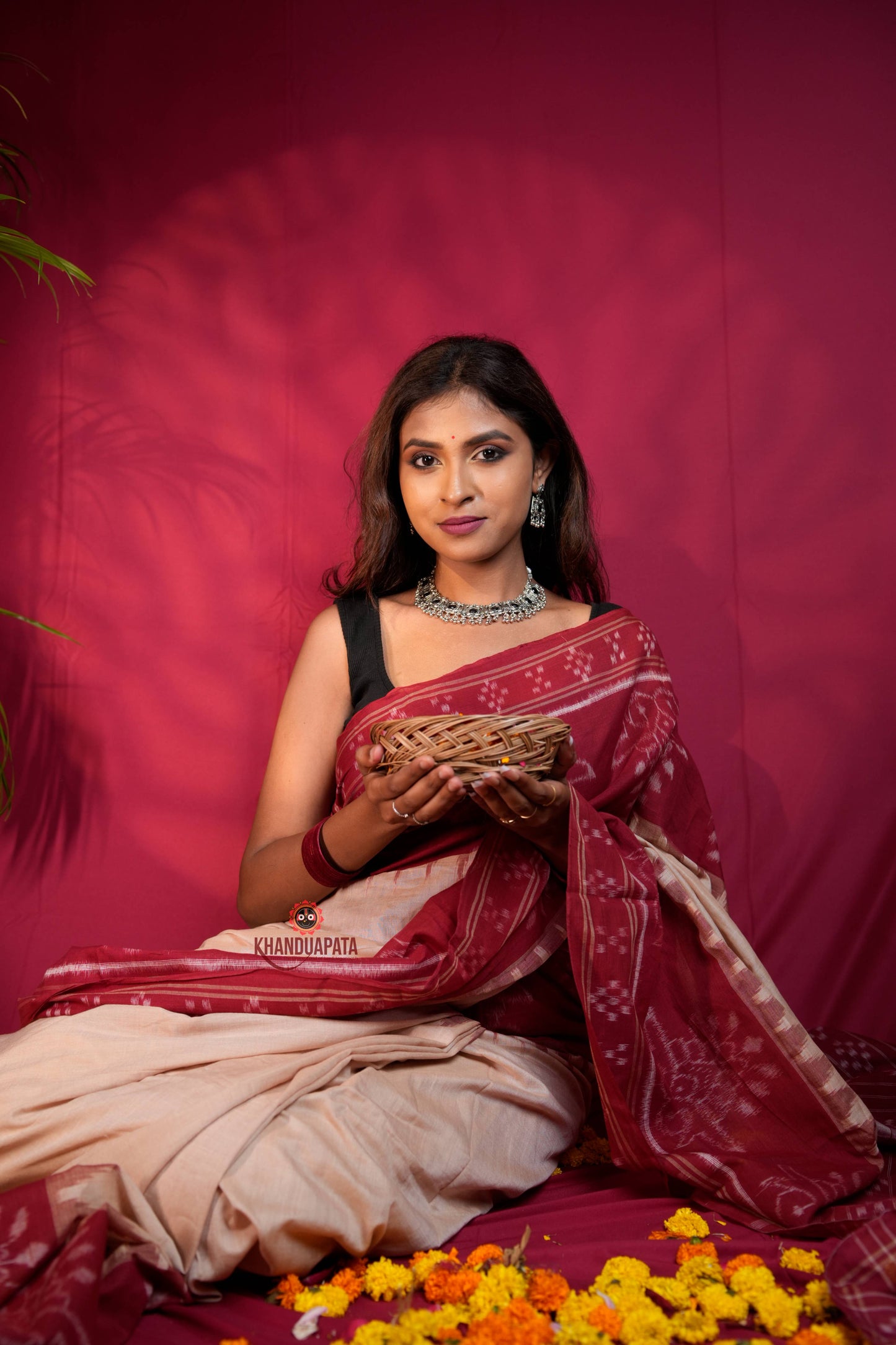Woman in a red saree holding a basket against a red background