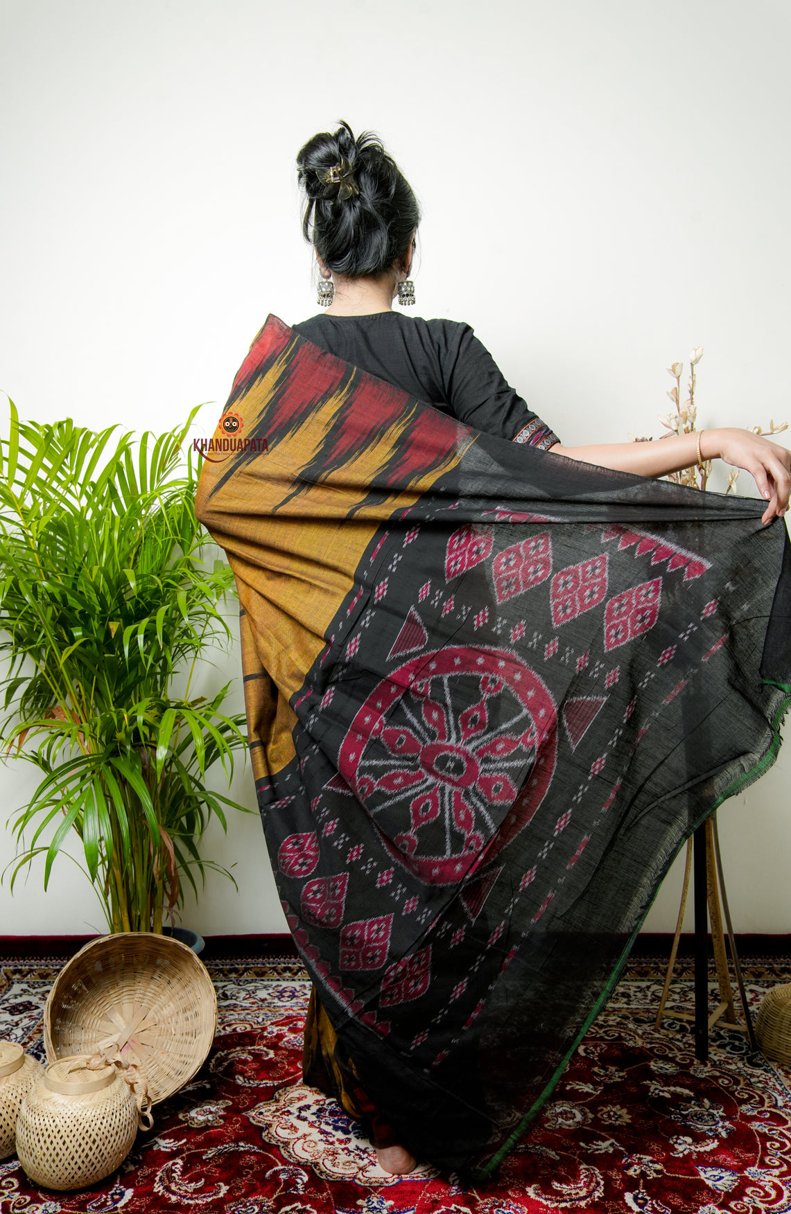 Woman holding a traditional patterned fabric with a plant and decorative items in the background