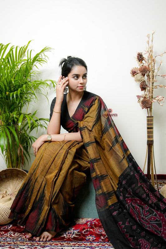 Woman in a traditional saree sitting on a patterned rug with plants in the background