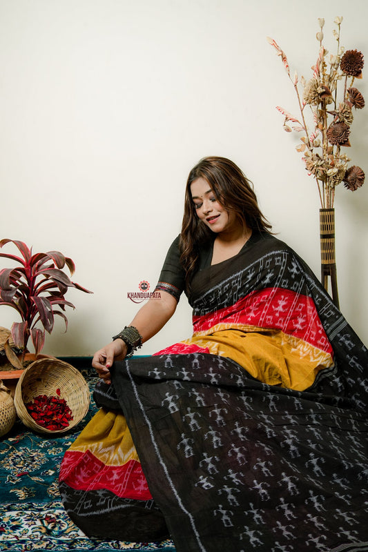 Woman wearing a traditional saree with a patterned design, sitting on the floor with decorative plants around.