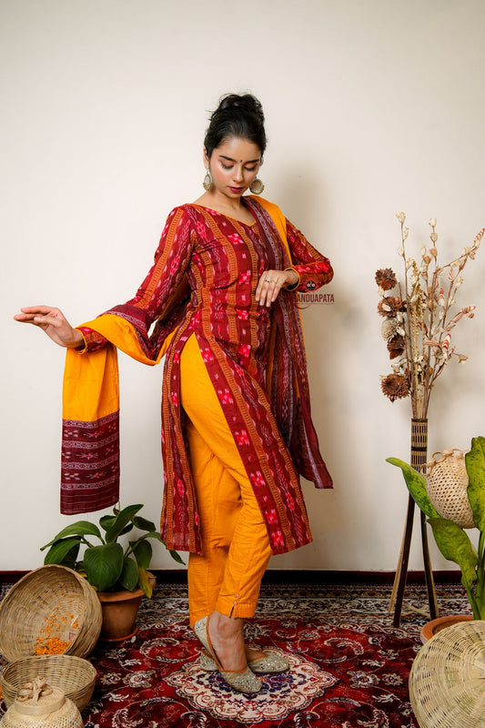 Woman in a maroon and yellow traditional outfit standing in a room with plants and decor.