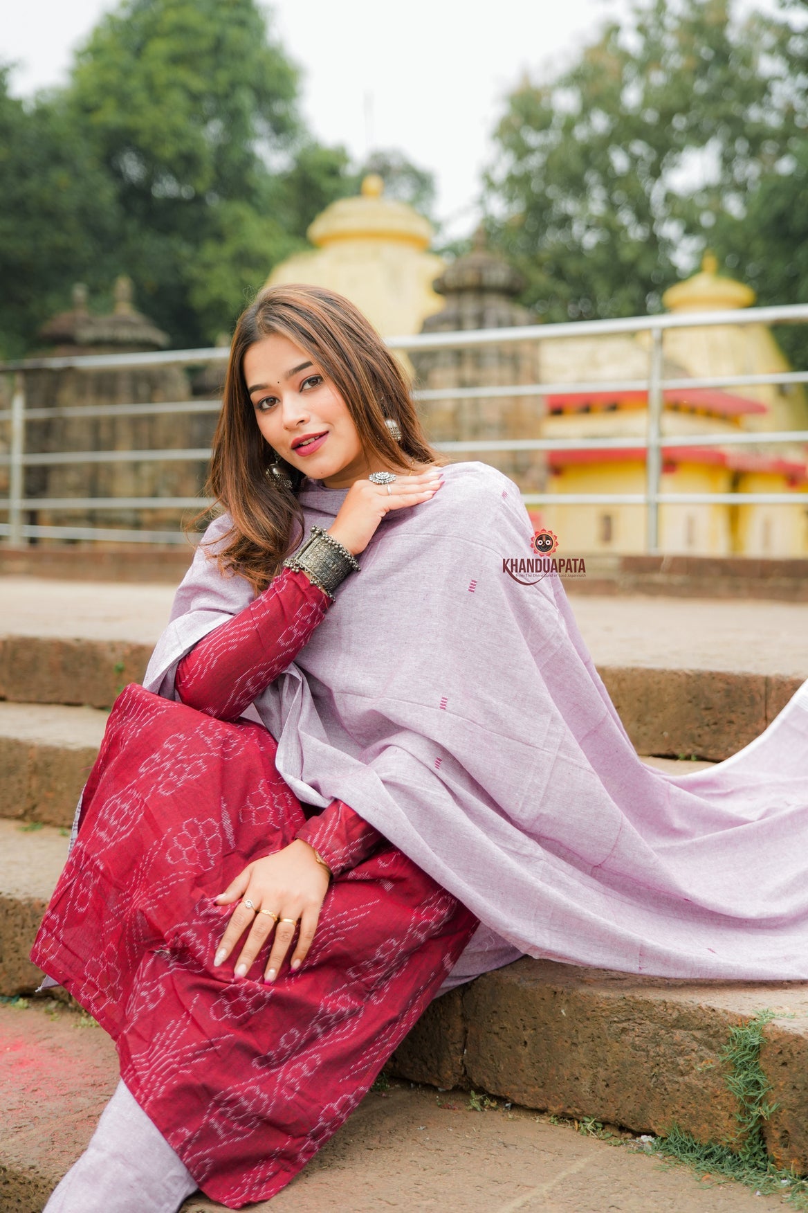 Woman in a pink and red traditional outfit sitting on steps with a temple in the background