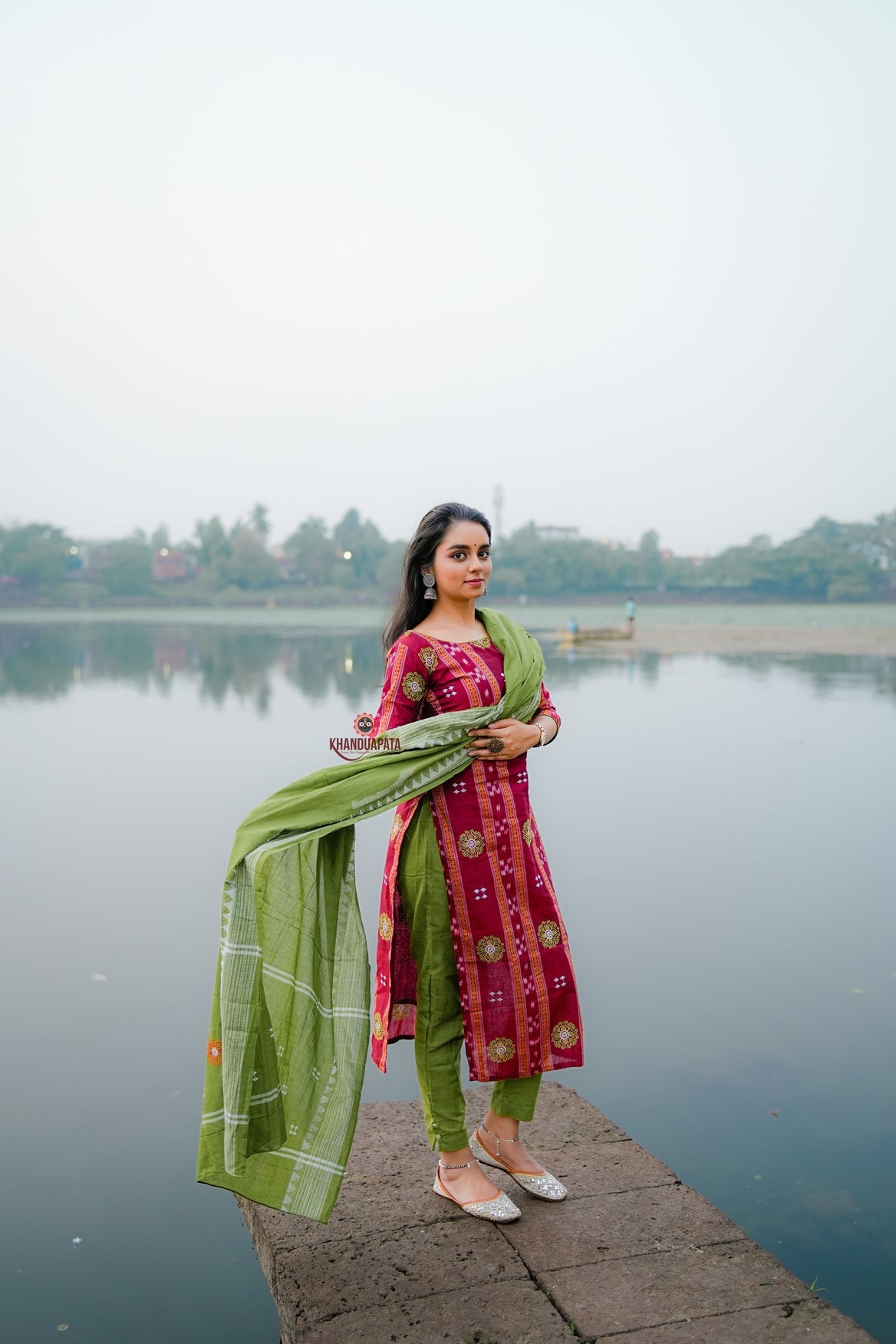 Woman in traditional attire standing by a lake