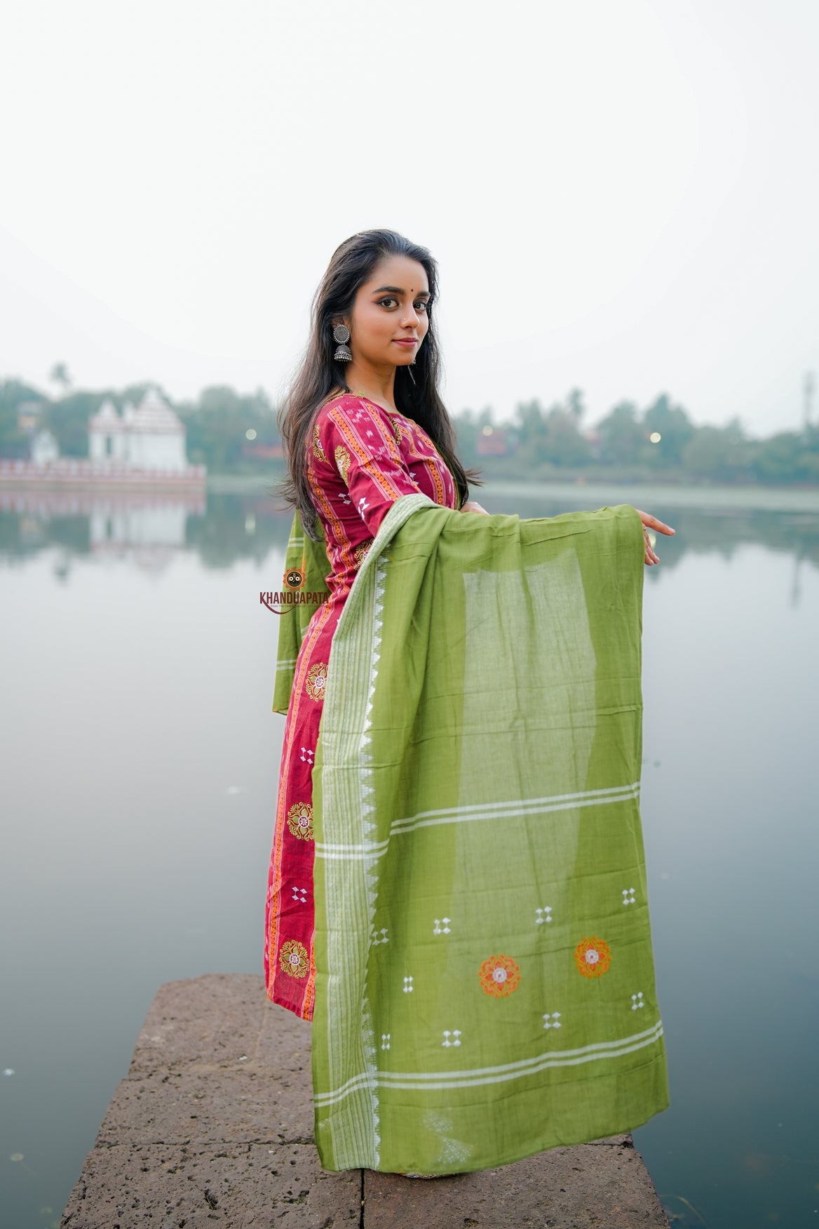 Woman holding a green saree by a body of water