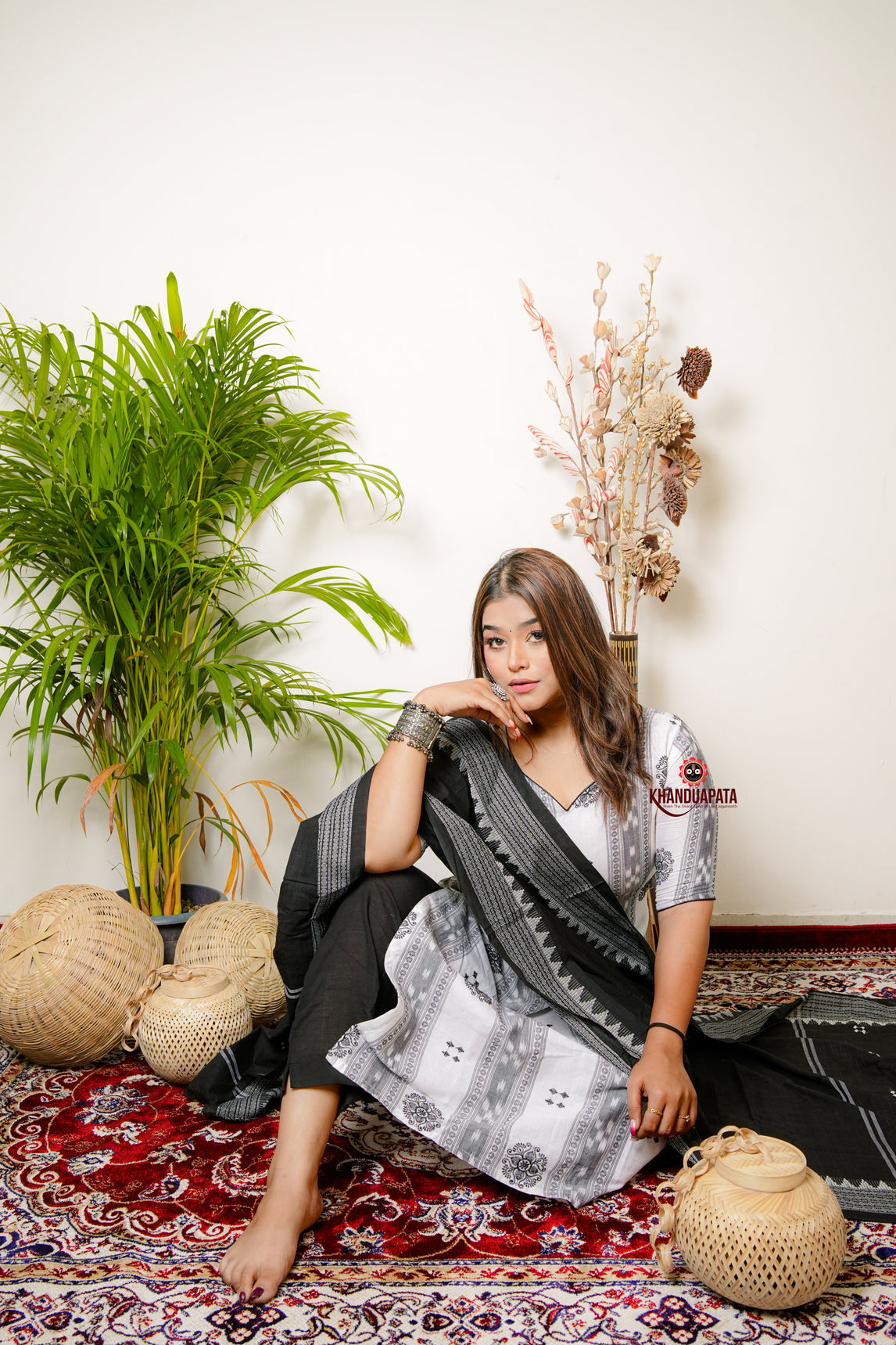 Woman sitting on a patterned rug with plants and decorative items around her