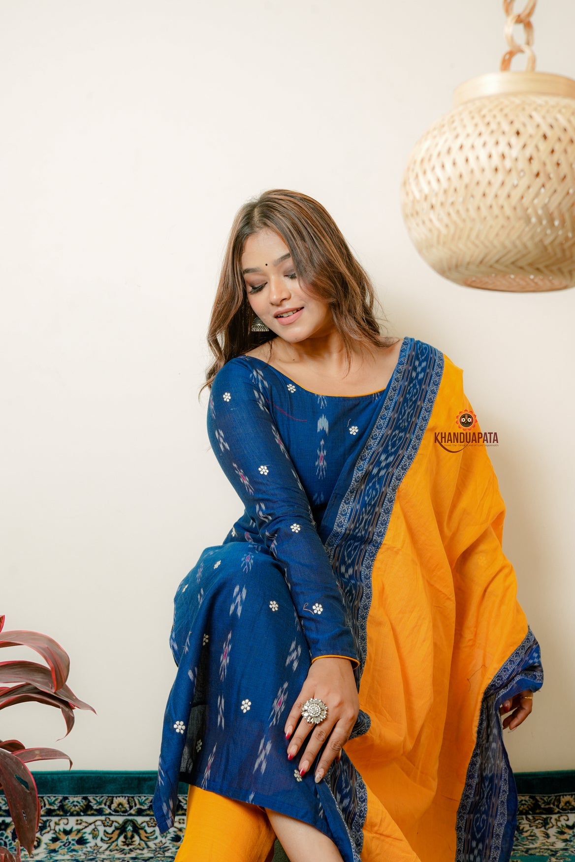 Woman wearing a blue and orange traditional outfit with a white wall background