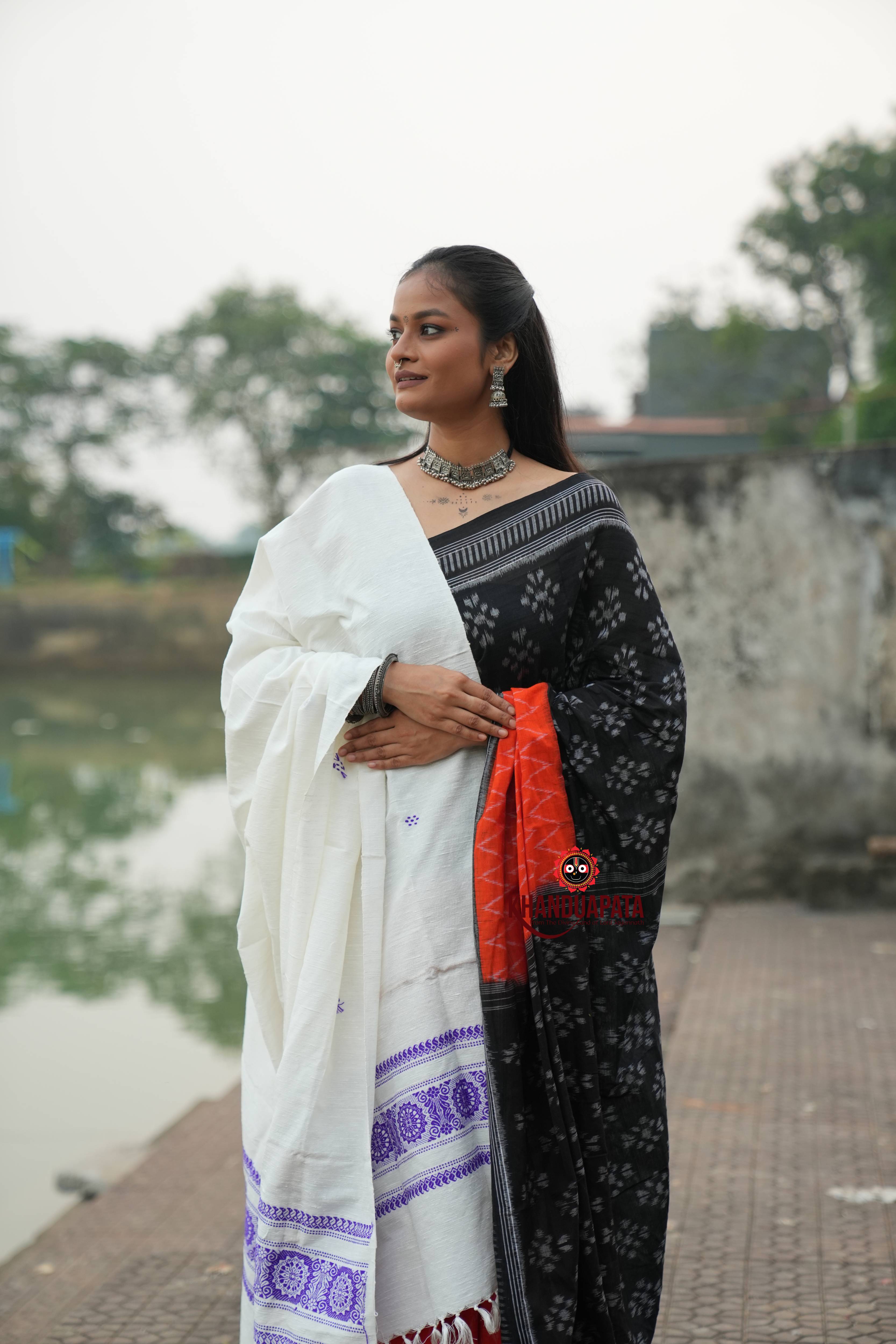 Woman in a black and white saree with a red blouse standing outdoors.