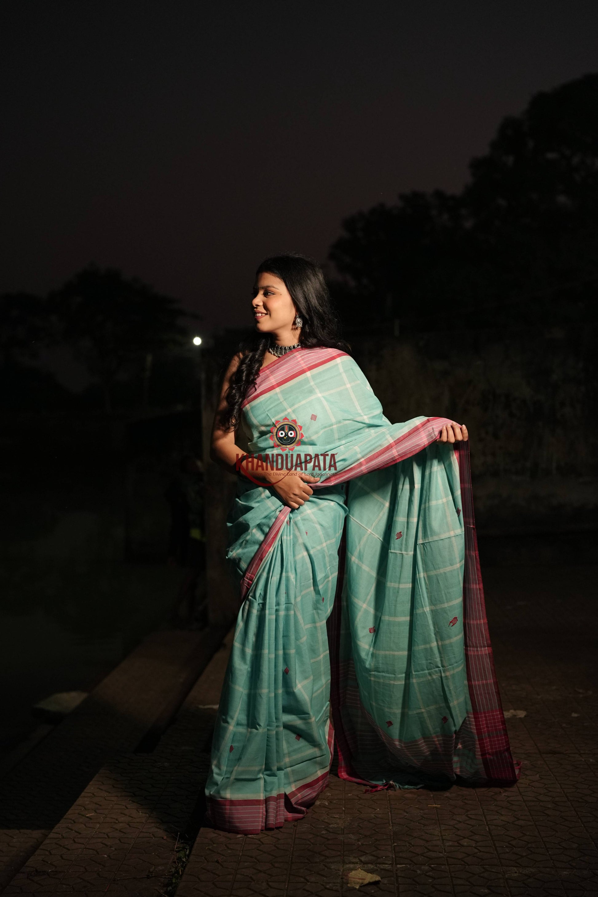Woman in a green saree with pink border standing outdoors at night.