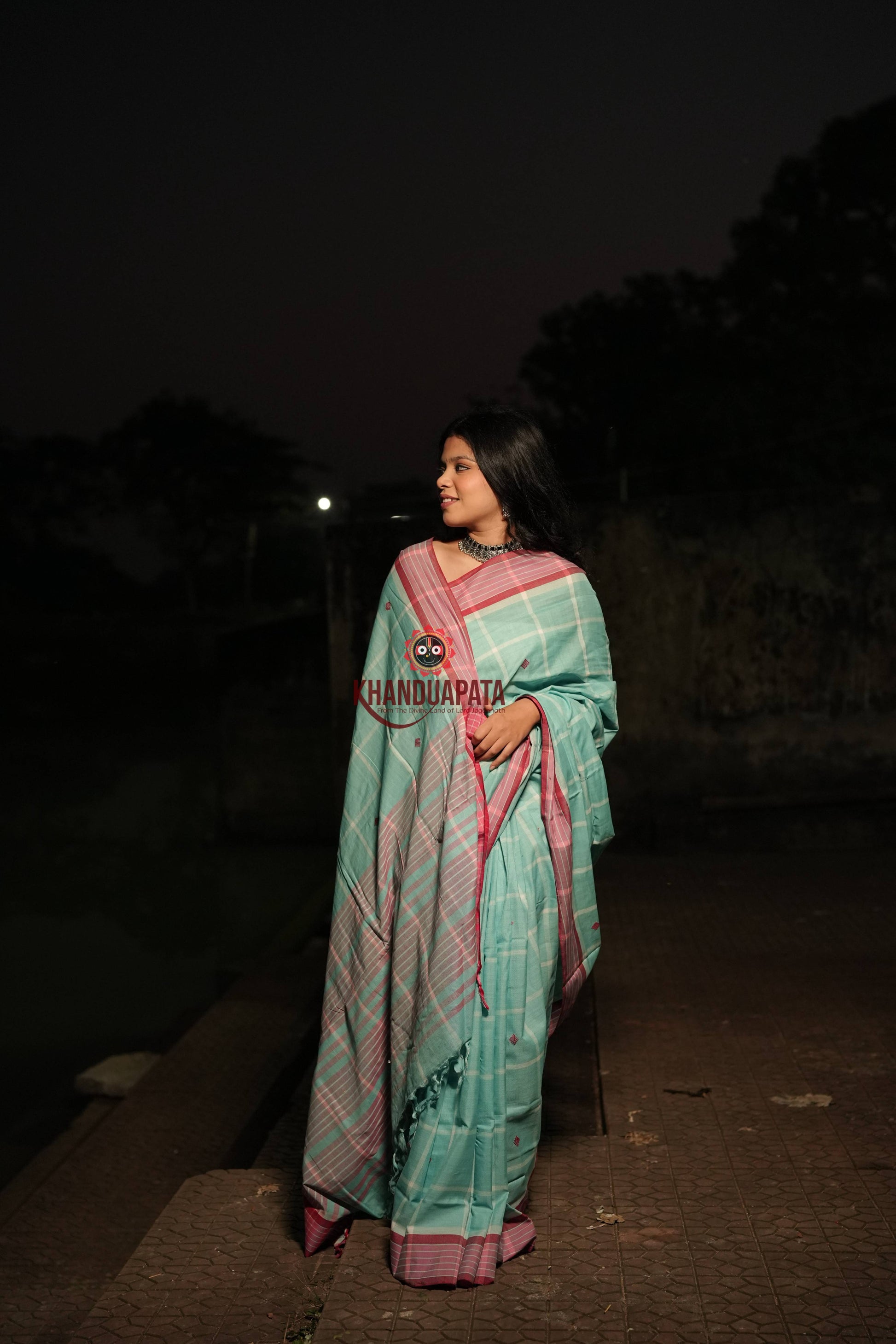 Woman wearing a light blue saree with pink border at night.