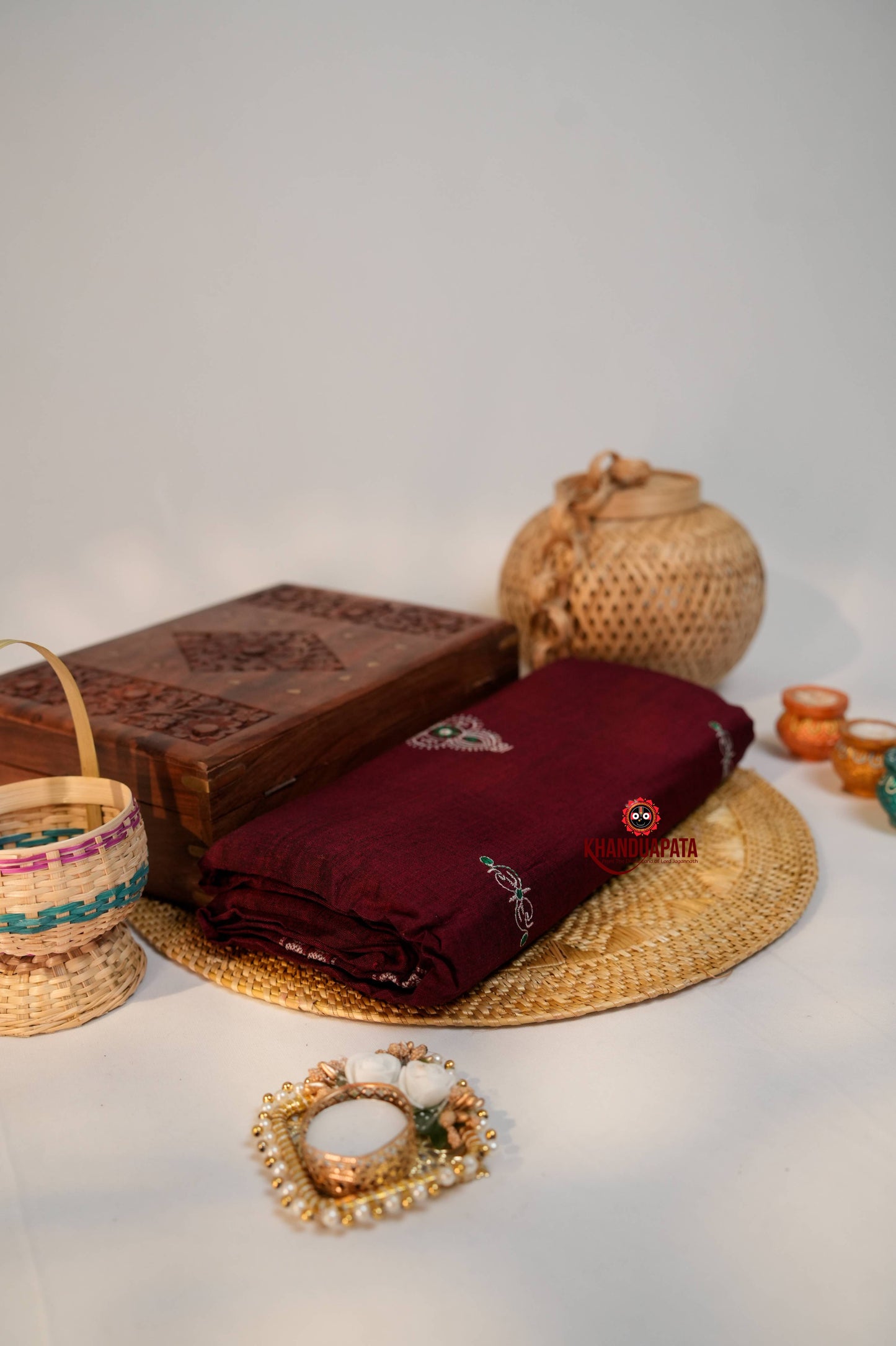 Maroon saree with embroidery on a woven mat, surrounded by decorative items.