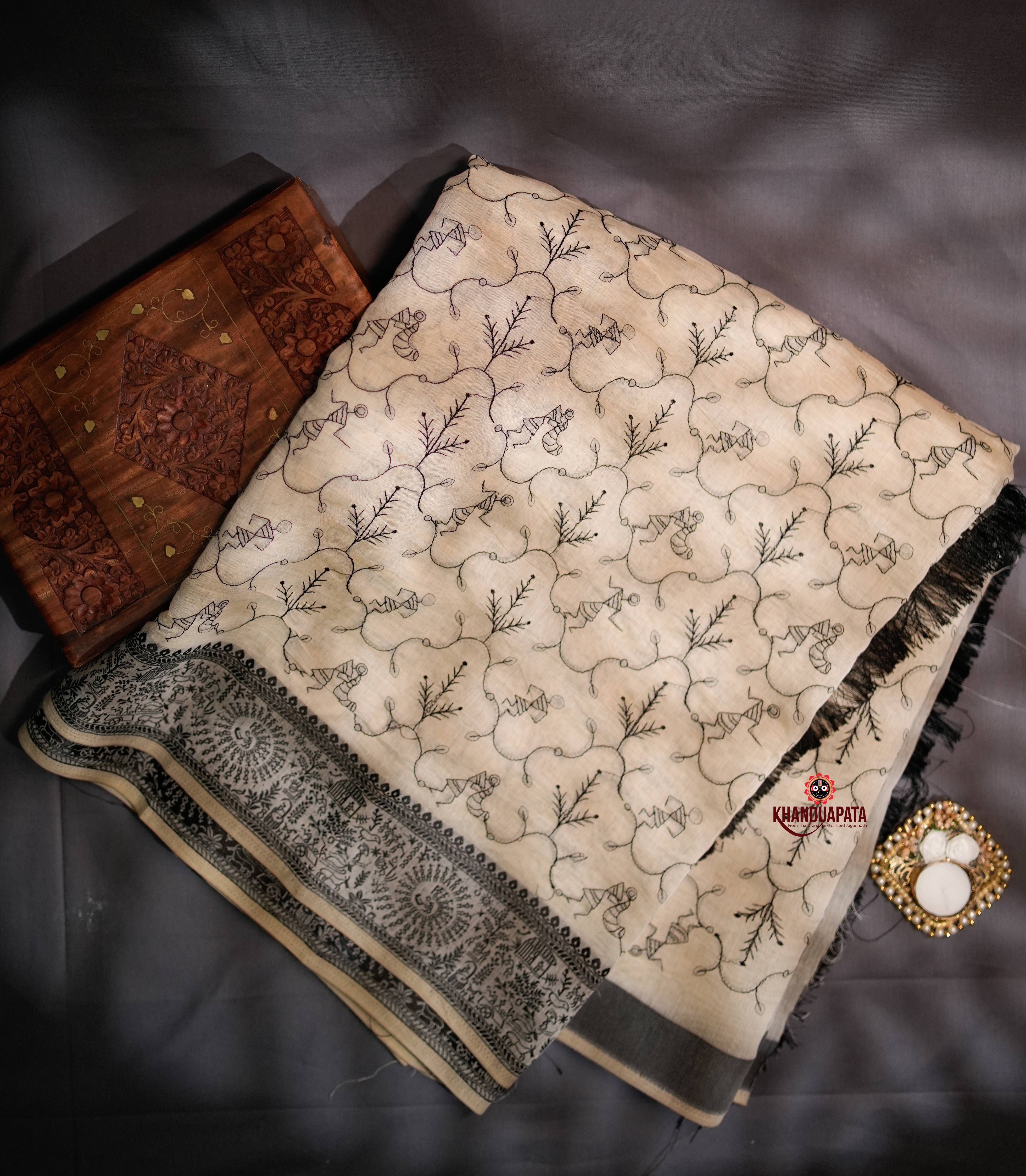 Embroidered fabric with intricate patterns on a dark surface, featuring a wooden box and decorative item.