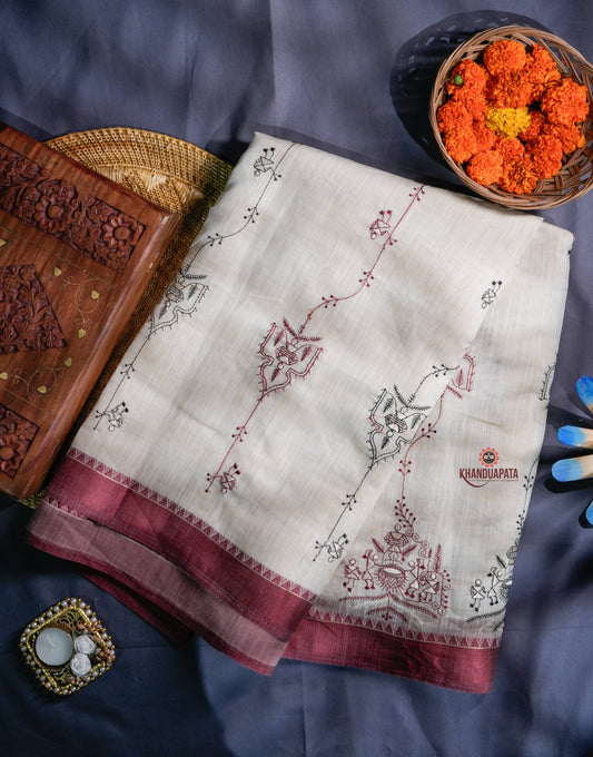 Embroidered fabric with maroon border on a blue fabric background, accompanied by decorative items.